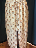 A beige maxi skirt with a brown and tan floral block print pattern, featuring an elastic waistband and a front slit, displayed on a mannequin against a dark background.